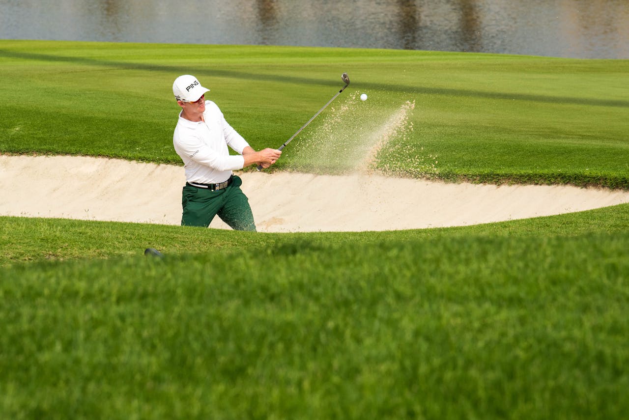 A golfer skillfully hitting a ball from a sand trap on a bright sunny day, showcasing sporting technique.