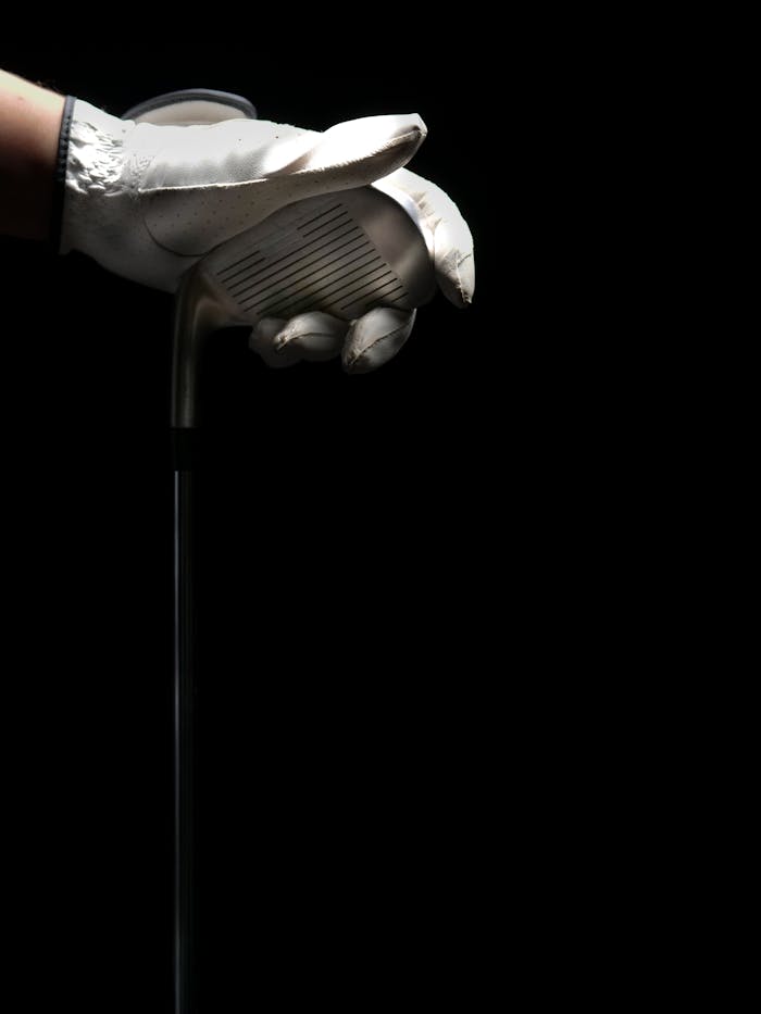 A gloved hand gripping a golf club against a dark background, symbolizing precision in sport.